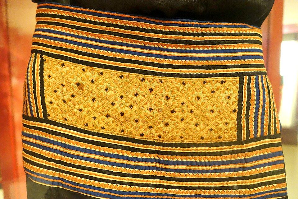 Close detail of a Hmong Den textile with yellow embroidery, batik, and geometric bands